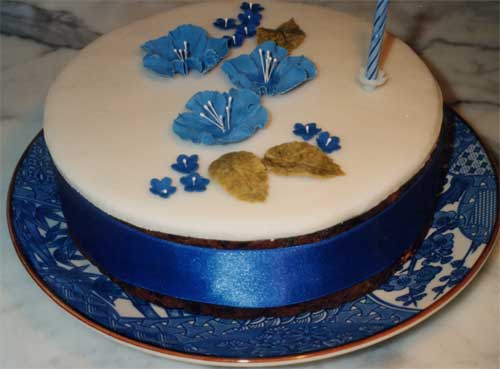 A simple cake decorated with blue and gold sugar crafted flowers and leaves.