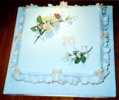 A 70th birthday cake.  A square rich fruit cake with sugar crafted floral decoration, frills and bows.