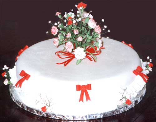 A cake prepared for a Ruby Wedding celebration, with red and white sugar crafted flowers, red bows and white frills.