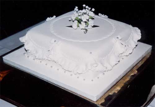 A Christmas cake decorated with sugar crafted holly and frills.Square cake with spray of white sugar crafted flowers for a Silver Wedding celebration.