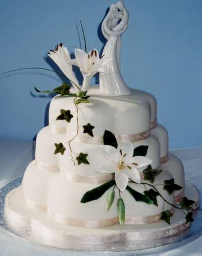 A three-tier, petal-shaped, stacked rich fruit cake, with sugar-crafted cream lilies and ivy.  The statuette was chosen by the bride.